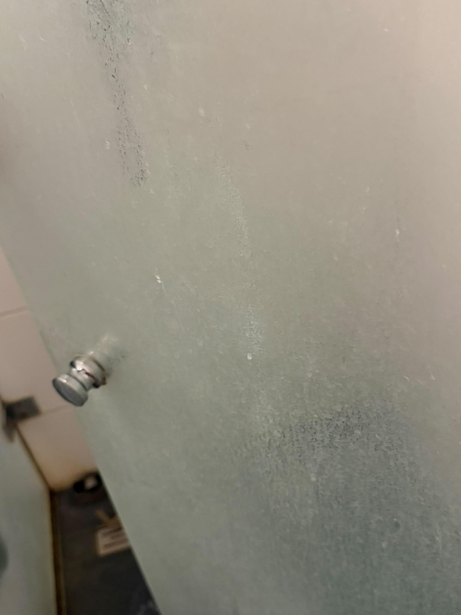 Glazen douchedeur vóór de deep clean, met vlekkerige aanslag rond de deurknop