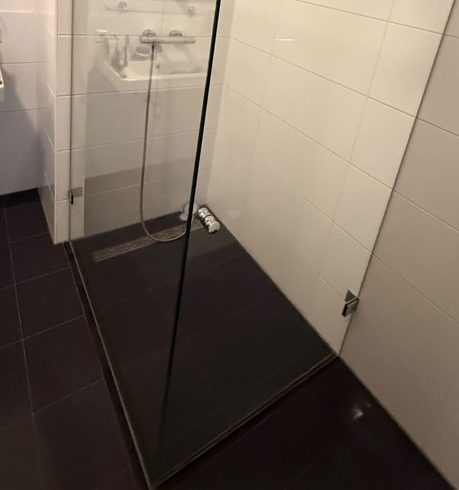 Glazen douchewand na de deep clean: helder glas met de douchekraan en witte wandtegels erachter