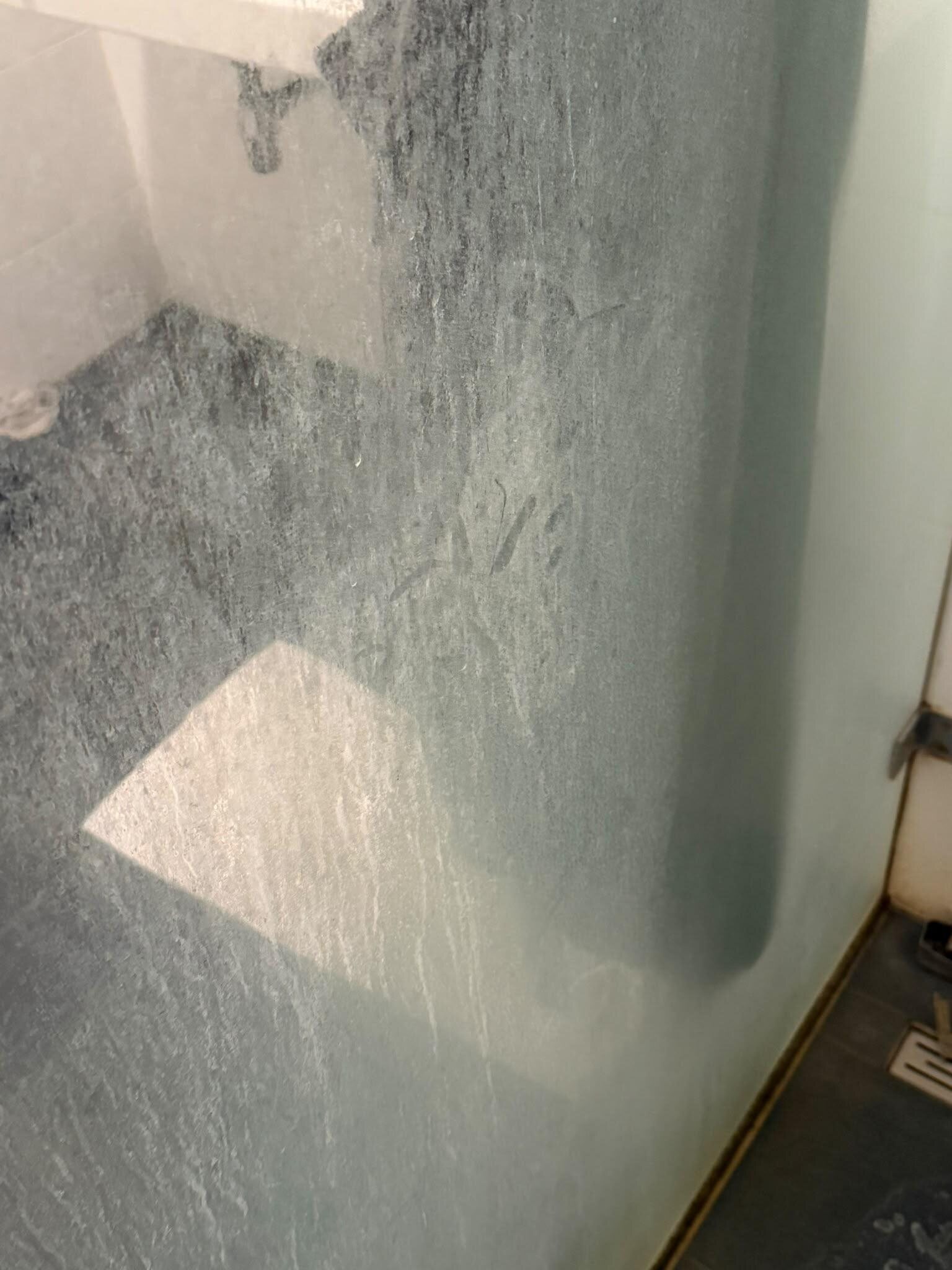 Glazen douchewand vóór de deep clean, bedekt met een witte aanslag waardoor het glas troebel is