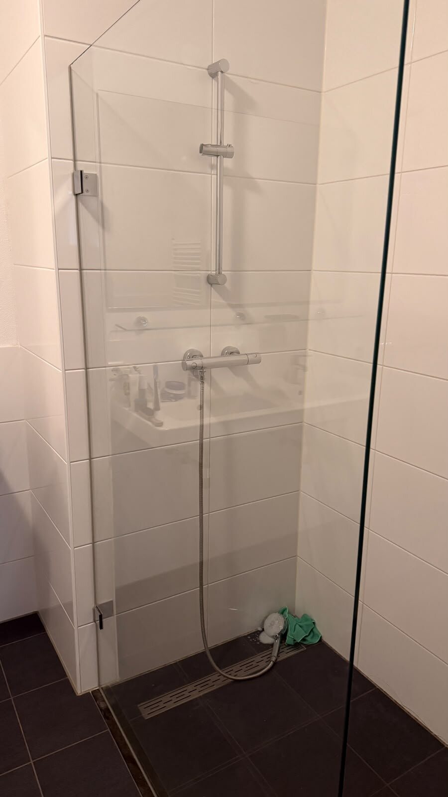 Douchehoek na de deep clean: witte wandtegels met lichte voegen, de glazen wand en de douchegoot
